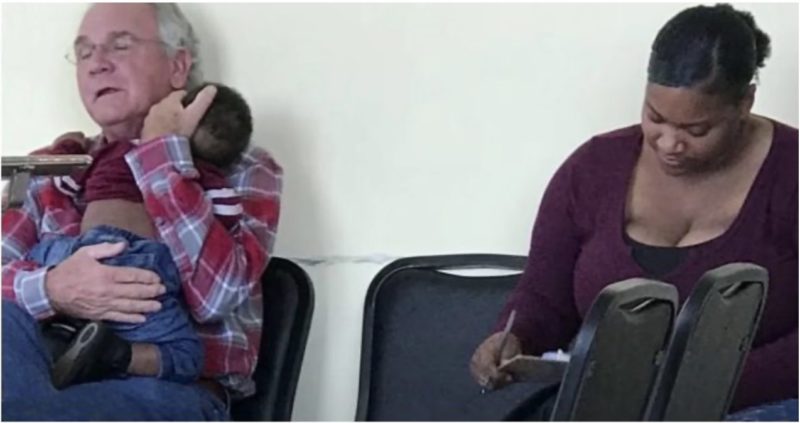 Un uomo tiene il bambino di una sconosciuta nella sala d'attesa affinché la madre possa compilare i moduli